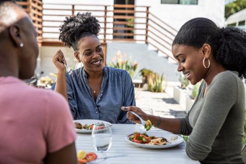 Three women gathering around a table laughing and sharing a meal