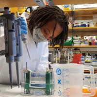 Woman in lab coat and mask leans over medical equipment